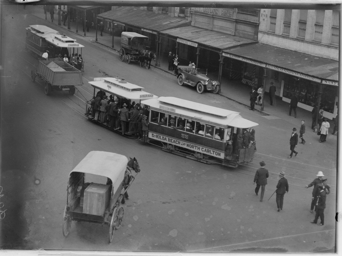 Truck towing tram in procession along street and view of shop fronts such as Reaby Taylor Pty Ltd and the Melbourne Cafe, Prahran (1902–20)
