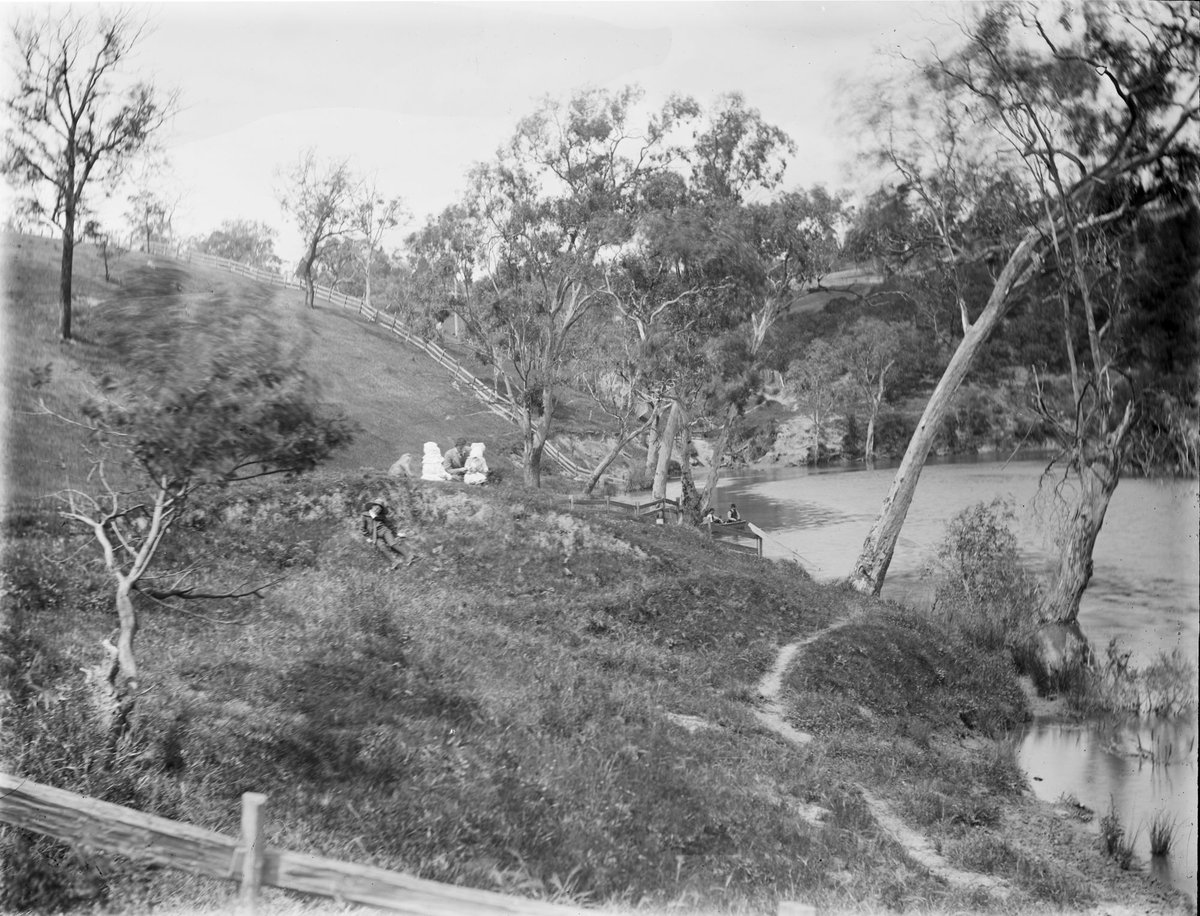 Men fishing, girls in bonnets on hill with pet monkey, possibly at the Yarra, Kew (1890–1910)