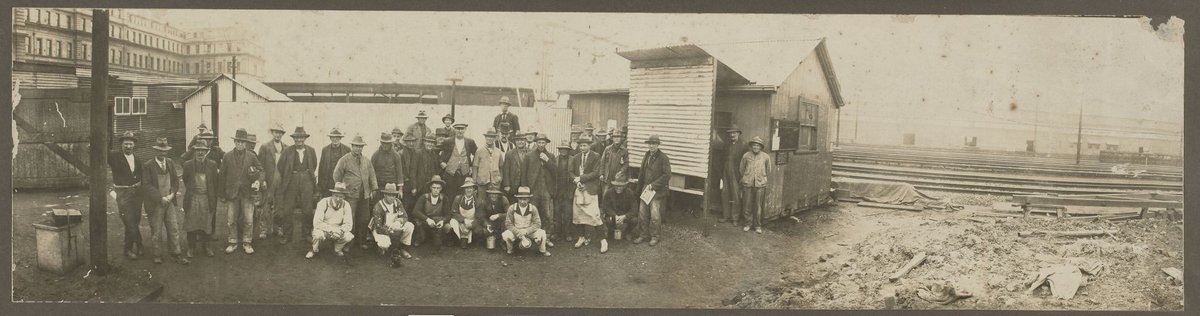 Group of men in workclothes posing in Spencer Street railway yards, Melbourne City (c. 1900)