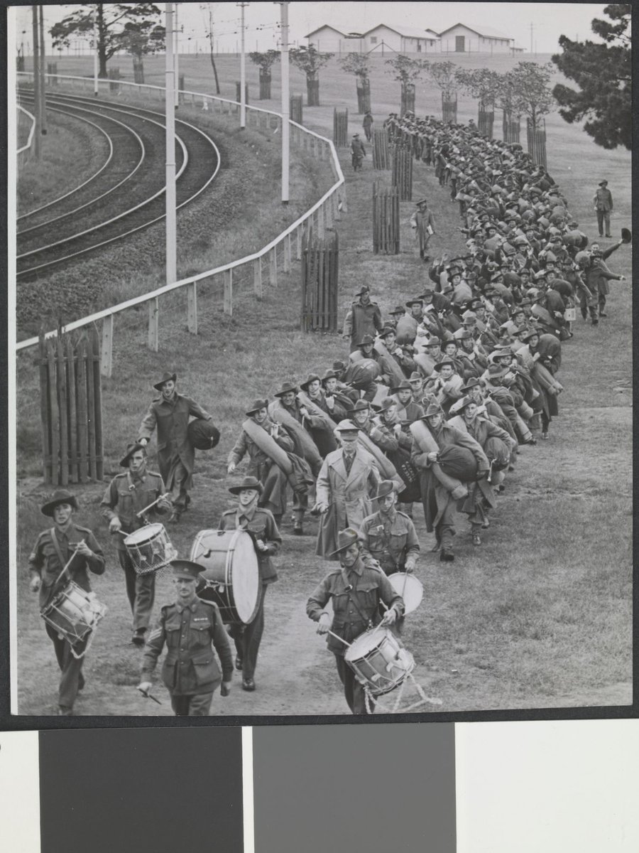 Troops marching behind drummers and officer along side tram or train tracks, Royal Park, Melbourne, Parkville (c. 1940)