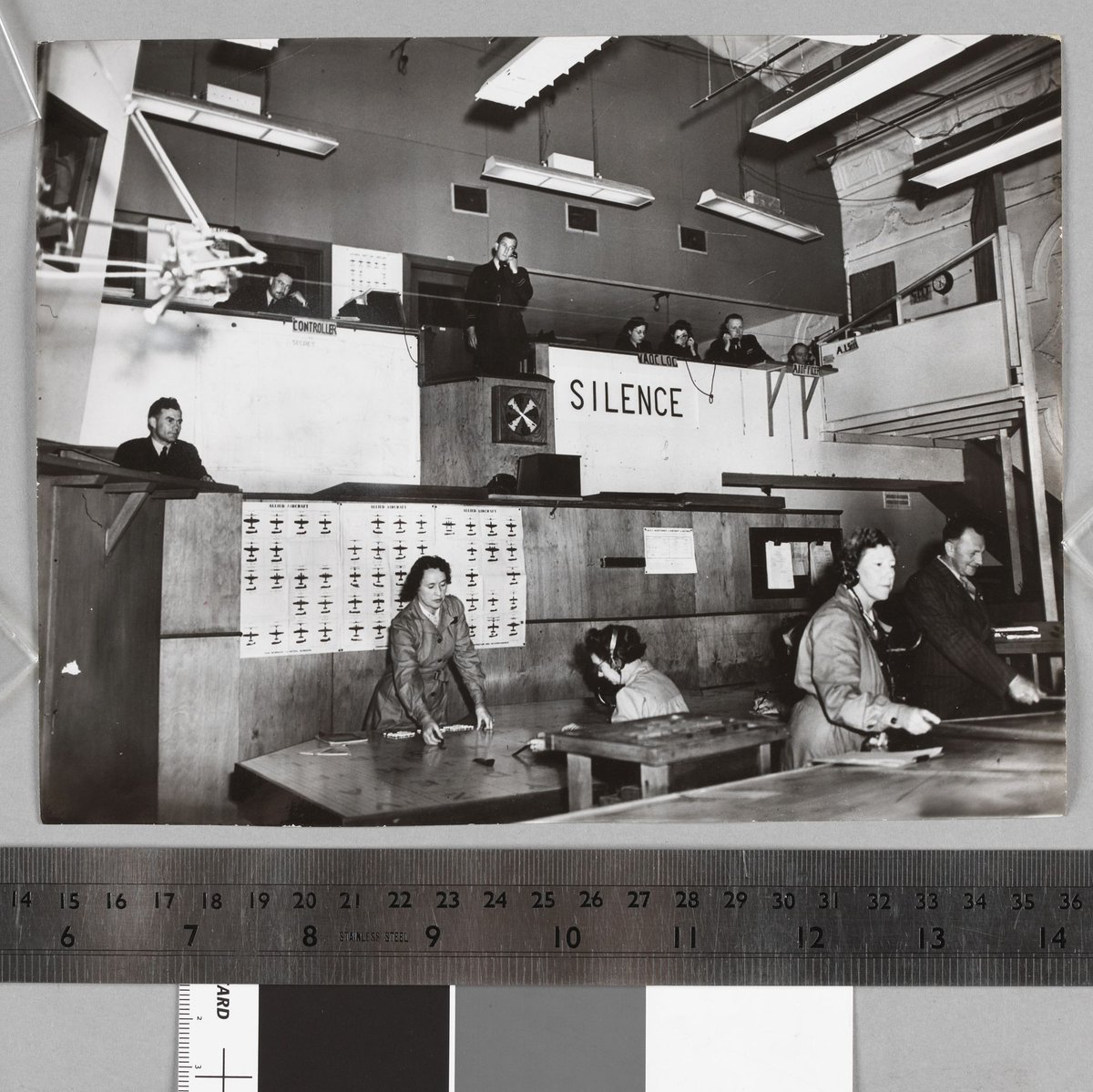 At the VAOC's nerve centre, a central air sector near Melbourne, the controllers balconies overlook the "plotting" table. A floor supervisor is on the first balcony watching operations. On the upper balcony are the male controllers, WAAAF liaison officers between VAOC and country centres and the identification centre (extreme right) (c. 1944)