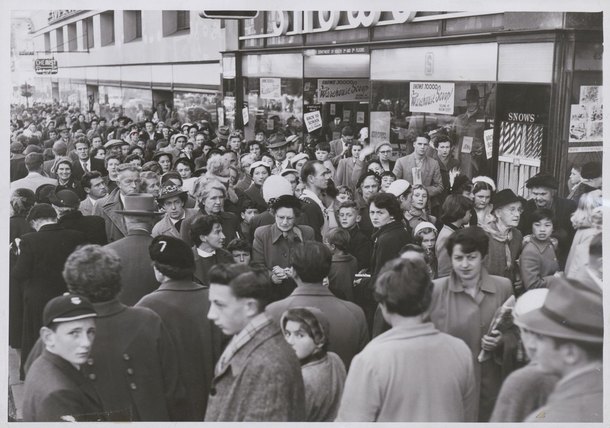Crowd consisting of women and small children waiting in a queue on the footpath, possibly to enter the Esquire Theatre, Bourke Street, Melbourne, Melbourne City (c. 1953)