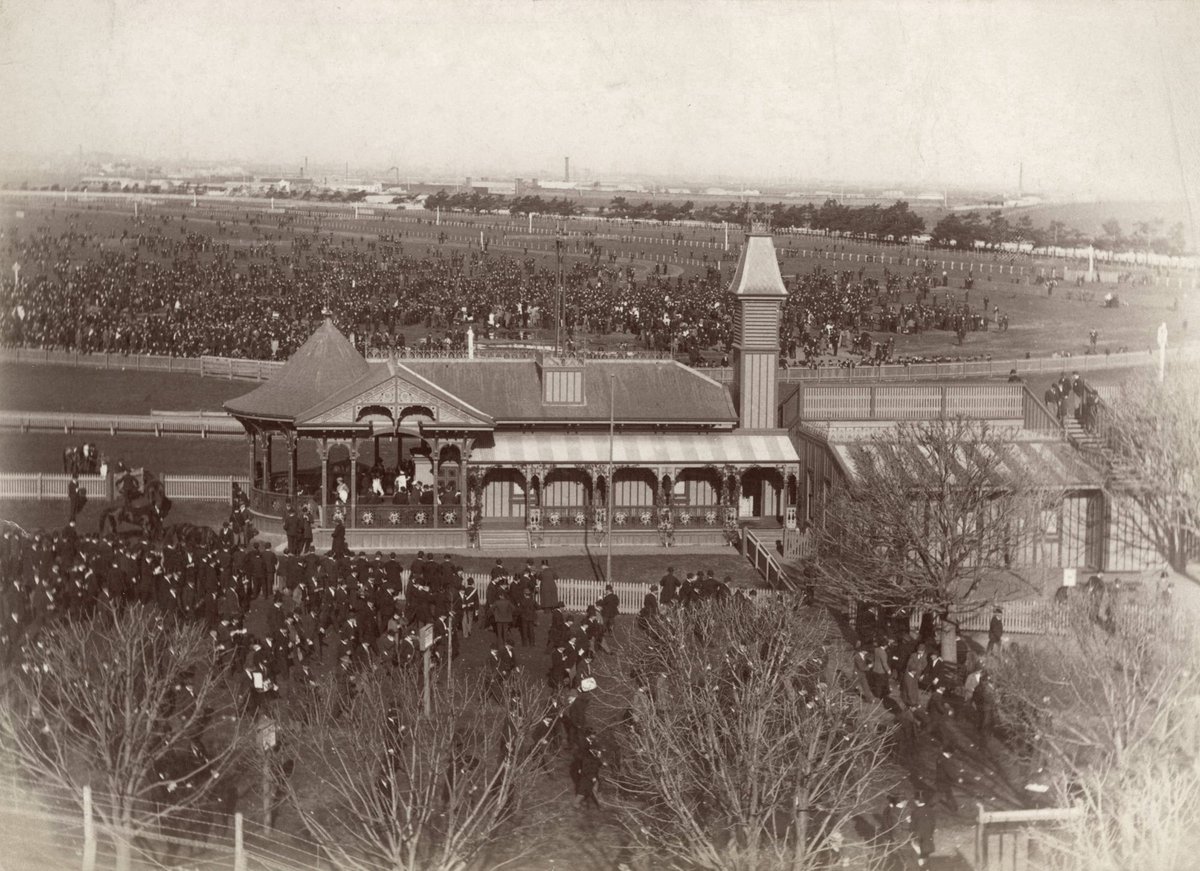 Race day at Flemington Race Course, showing crowds in centre of track and back of grandstand (1890–1900)