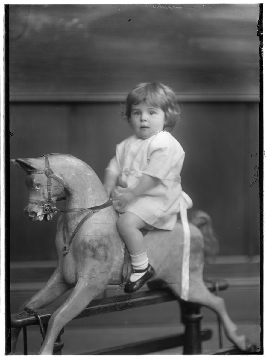 Studio portrait of child sitting on carved wooden glider rocking horse, surname possibly Hampton (1920–30)