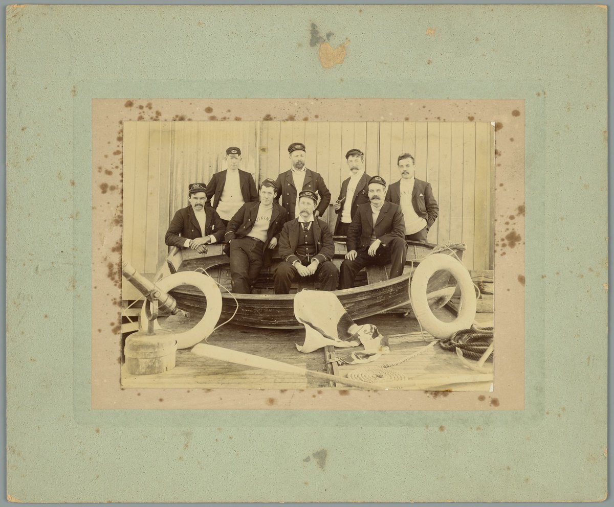 Whole-length portrait of eight men in nautical clothing with wooden dinghy, possibly at Williamstown (1900–10)