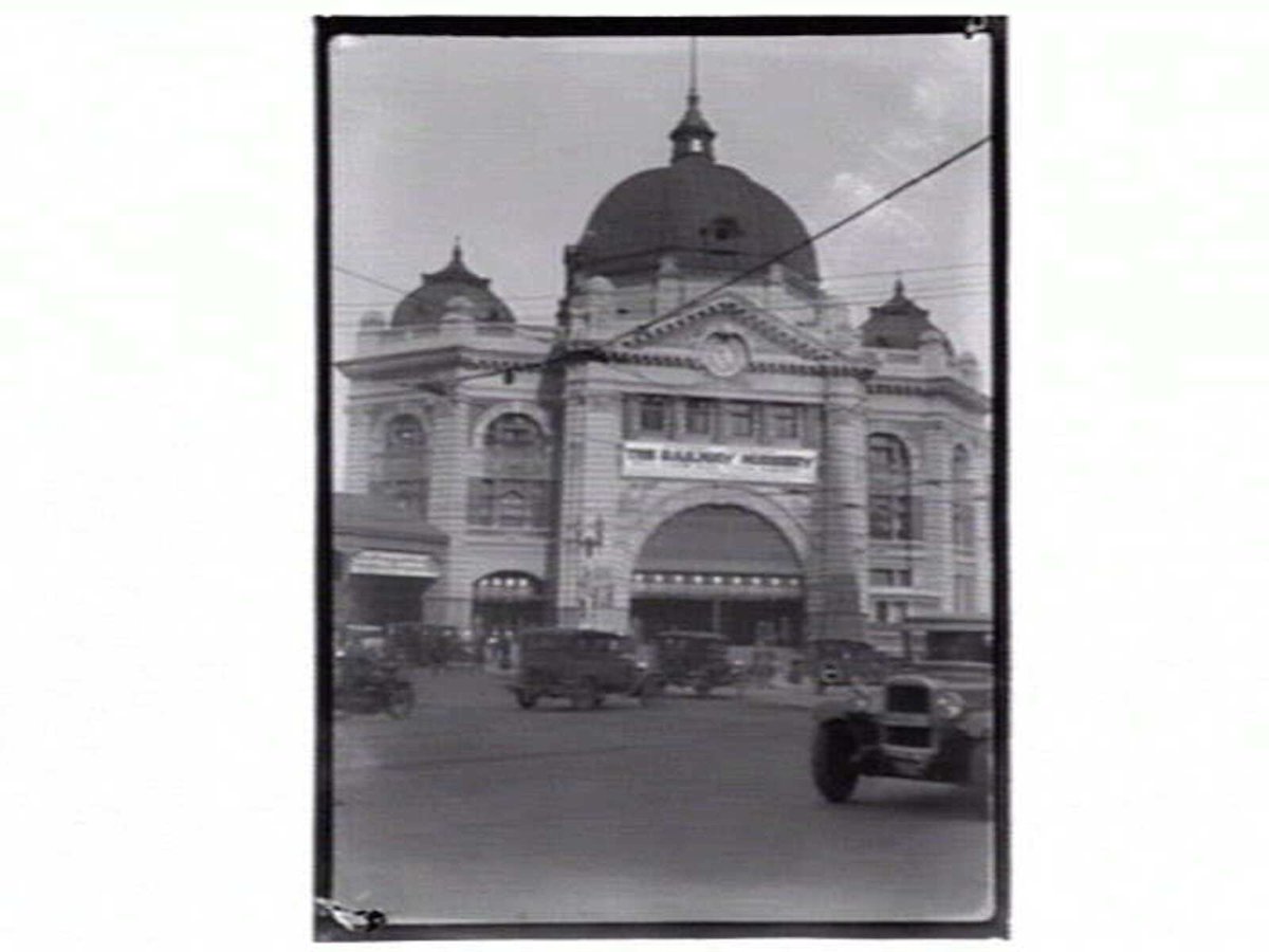 Flinders Street Station with cars and sign "The Railway Nursery", Melbourne City (1914–33)