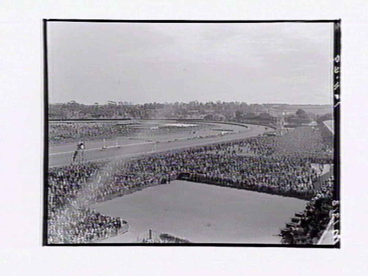 Bird's-eye view of Flemington Racecourse, showing crowd around mounting yard, racetrack in distance, Melbourne Cup Day (1949)
