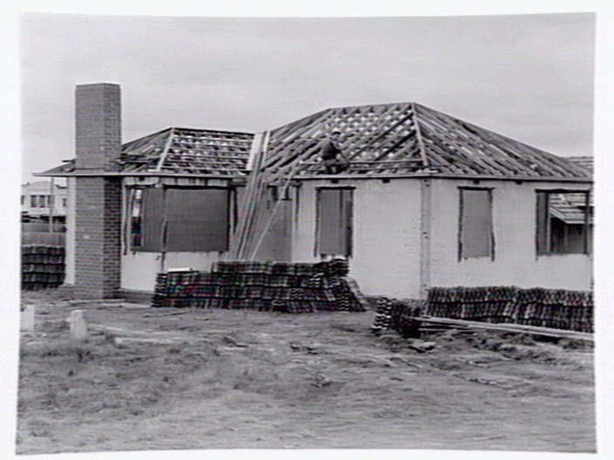 Housing Commission estate homes under construction at Ashburton, showing stumps, roof before tiling and cranes putting up concrete, pre-fabricated walls (c. 1946)