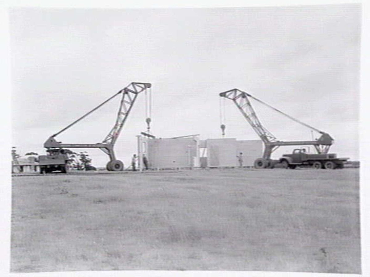 Housing Commission estate homes under construction at Ashburton, showing stumps, roof before tiling and cranes putting up concrete, pre-fabricated walls (c. 1946)