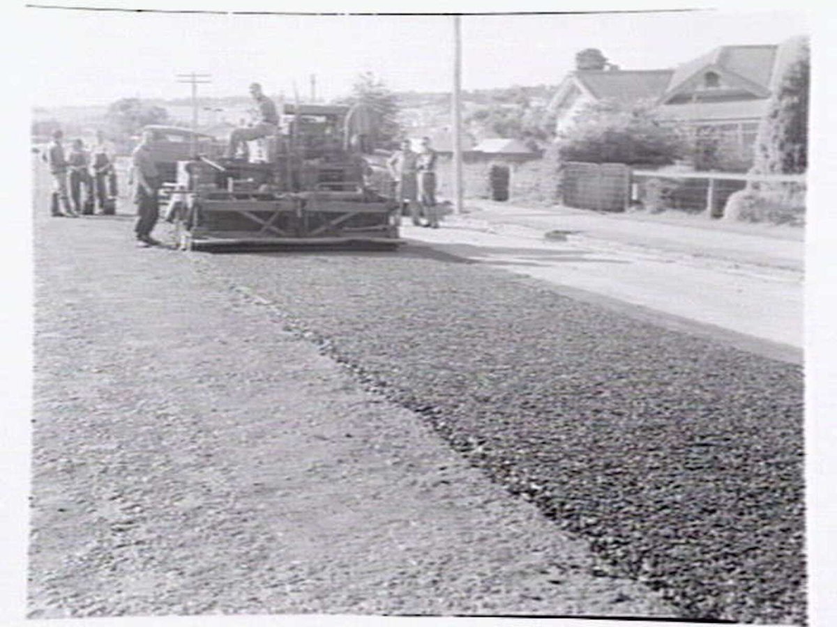 Roadmaking by Albion Quarrying P/L, showing machine laying asphalt and section of road in Heidelberg yet to be resurfaced (1950)