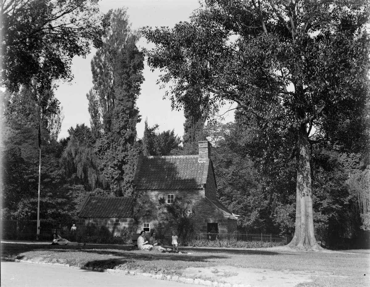 Family sitting in garden at Cook's Cottage, Fitzroy Gardens, East Melbourne (c. 1934)