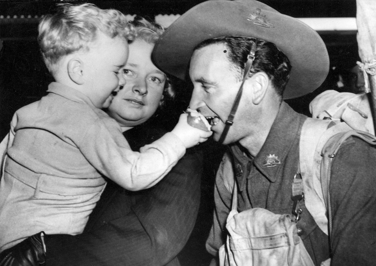 Driver John Oates, returned from overseas greeted by Robert and Mrs. Oates at Spencer St[reet Station, Melbourne] & a bite of Robert's apple, Melbourne City (c. 1942)