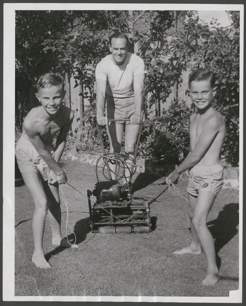 Looking after Dad, Ian Johnson gets a helping hand from his sons to cut the lawns before going down to Albert Park beach for a swim (1954)