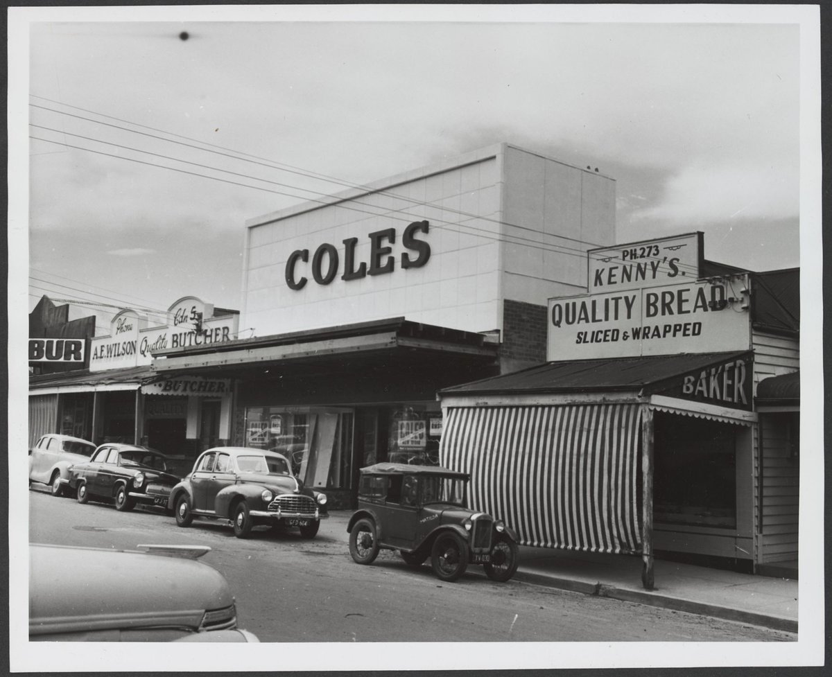 Row of shops with cars parked at curb including baker with striped awning adjoining Coles Croydon Store No. 204 (1935)