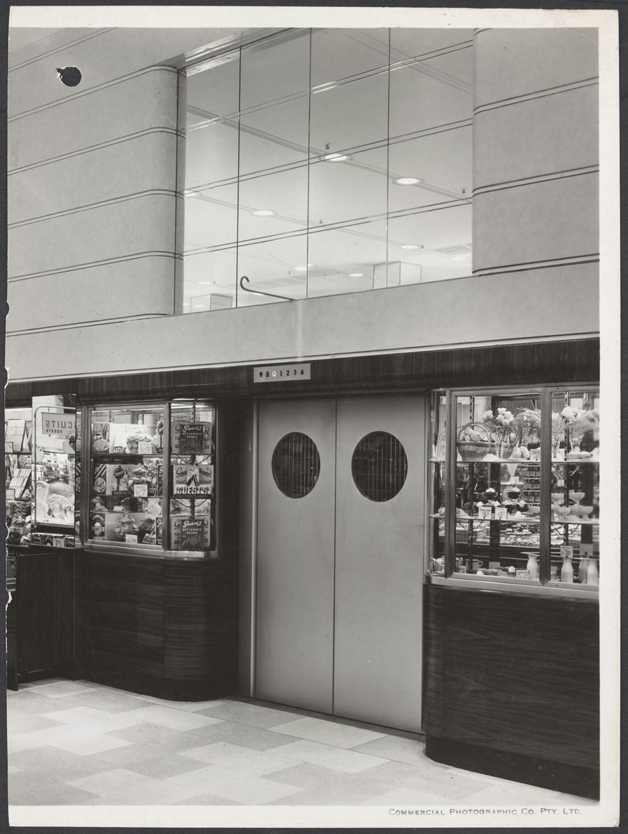 View of lift doors flanked by cabinets displaying food in Coles Bourke Street Store No. 12, Melbourne City (1940–47)