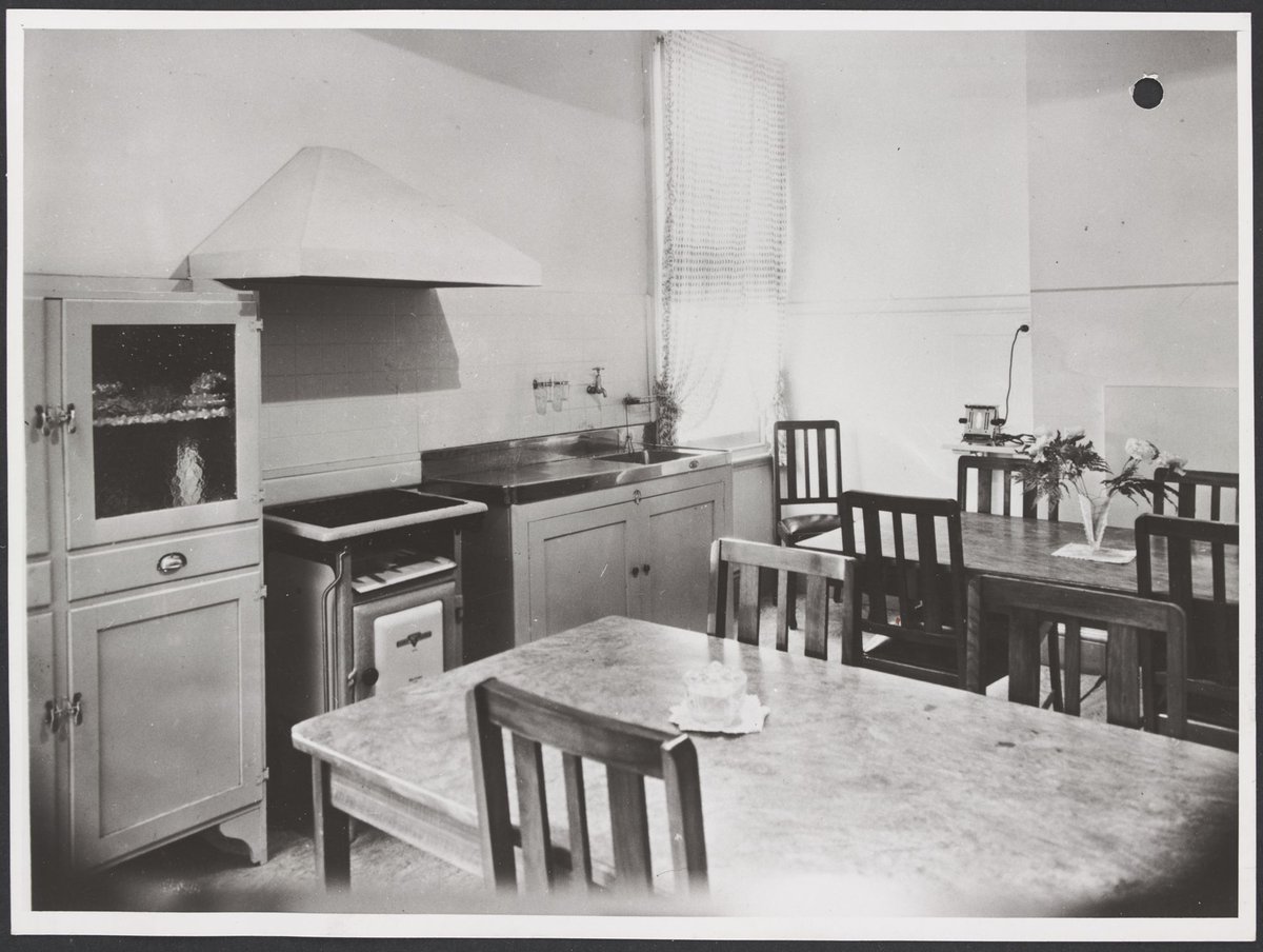 Kitchen with two wooden dining tables, chairs, stove, sink and cupboards 411-415 Sydney Road Brunswick Store No. 3 (1947)