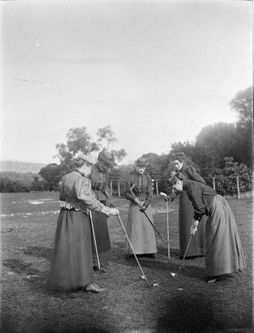 Women members at the old Kew Golf Club, Mrs. Anderson second from right, all standing in circle with clubs watching one woman putting, 1890–1910