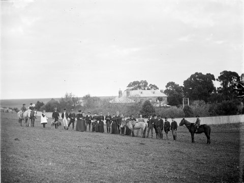 Hunt Club on River Flats at Kew. Group of men, women and children, some with horses, standing in a line, 1890–1910