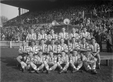 North Melbourne Football First Eighteen, (VFL) team in front of a grandstand, 1949–50