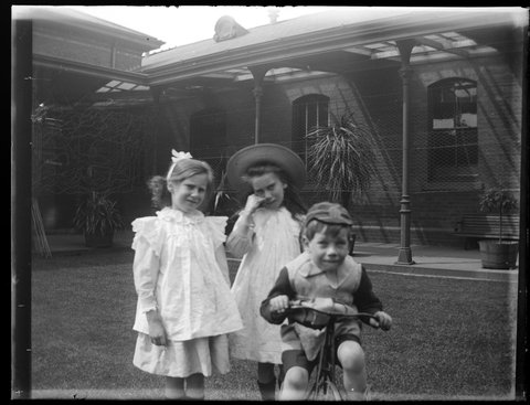 Clare and Gertrude (Peggy) with Vincent on tricycle, in Melbourne Mint quadrangle, c. 1906