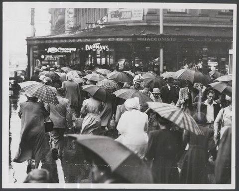 Sudden downpour in Melbourne streets. A sea of umbrellas appeared on the corner of Collins and Swanston Streets, 1953