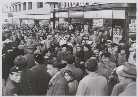 Crowd consisting of women and small children waiting in a queue on the footpath, possibly to enter the Esquire Theatre, Bourke Street, Melbourne, c. 1953