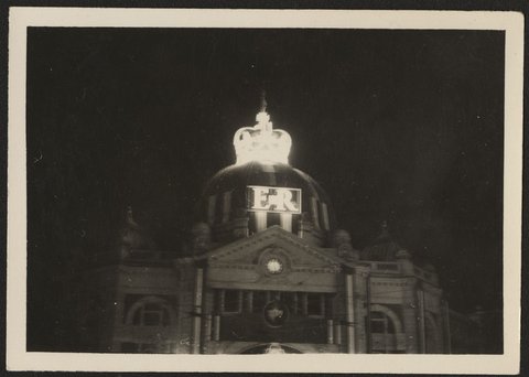 Night view of Flinders Street Station showing floodlit crown and letters ER at top of the dome, 1954