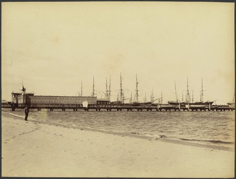 View from the beach of sailing ships at wharf, pier and baths, man standing on beach, possibly Port Melbourne, 1888?
