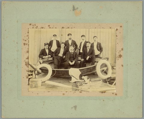 Whole-length portrait of eight men in nautical clothing with wooden dinghy, possibly at Williamstown, 1900–10