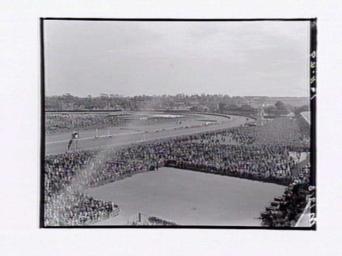 Bird's-eye view of Flemington Racecourse, showing crowd around mounting yard, racetrack in distance, Melbourne Cup Day, 1949