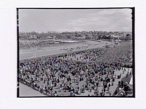 Bird's-eye view of Flemington Racecourse showing people watching horserace on Melbourne Cup Day, 1949