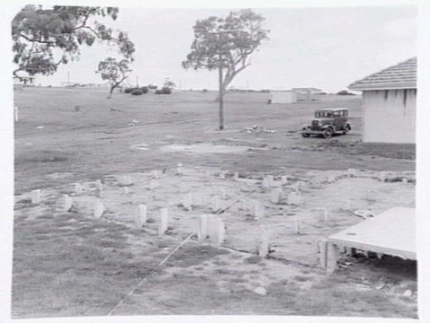 Housing Commission estate homes under construction at Ashburton, showing stumps, roof before tiling and cranes putting up concrete, pre-fabricated walls, c. 1946