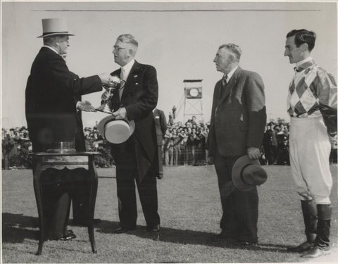 Mr A. E. Underwood, owner of Cup winner, Wodalla, receives the Melbourne Cup from the Governor-General (Sir William Slim), at his right is jockey Jack Purtell and next to him, trainer R. Sinclair, 1950–56