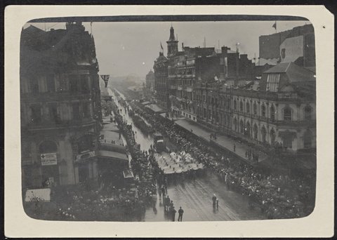 Elevated view of a rain washed Swanston Street looking towards Flinders Street from Town Hall roof: showing large crowd watching parade, marchers under flag, 1918