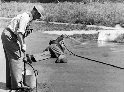 Man lying on road hosing a 'incendiary bomb' in Brighton during A.R.P. tests, c. 1942