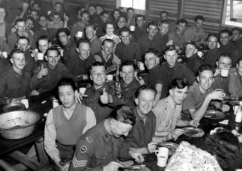 Troops smile and raise cups while eating Christmas dinner provided by members of the Royal Park Camp Women's Auxiliary, 1940–46
