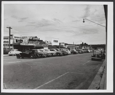 Looking across street and parked cars towards row of shops including Coles Croydon Store No. 204, 1935