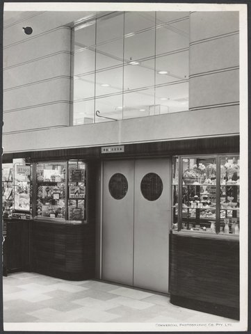View of lift doors flanked by cabinets displaying food in Coles Bourke Street Store No. 12, 1940–47