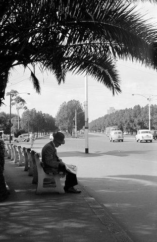 Man sitting on park bench next to St. Kilda Road, near entrance to Alexandra Gardens, Melbourne, 1954