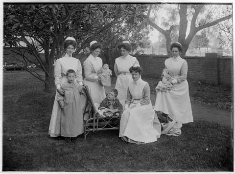 Nurses with babies and children, possibly in the red-walled garden at the Children's Hospital, Rathdowne Street, Carlton, 1890–1900