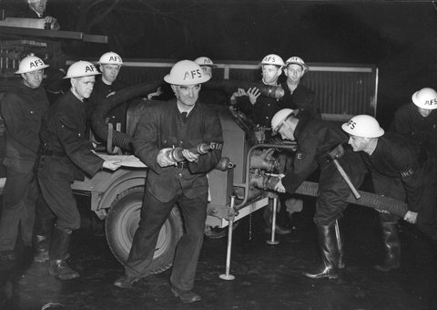 Fireman J. Godfrey of the Auxiliary Fire Service (Northcote Branch) holding fire hose attached to trailer pump, 1939–45