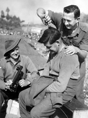 Time of for a trim, Private Jeff Binder, of Hawthorn (VIc.) watches the unofficial, inexperienced barber of the unit, 1950