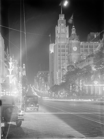 Collins Street looking west from beyond Swanston Street, showing Town Hall, Manchester Unity and APA Buildings illuminated as well as Centenary street poles, for Victoria's Centenary celebrations, 1934–35